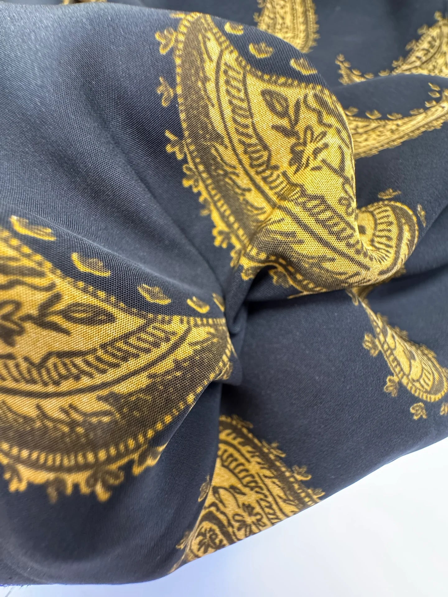 Bild mit italienischem 100 % Viskose-Chiffonstoff mit goldenem Paisley-Muster auf schwarzem Hintergrund – online erhältlich bei Šarlotes audumi