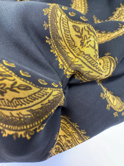Bild mit italienischem 100 % Viskose-Chiffonstoff mit goldenem Paisley-Muster auf schwarzem Hintergrund – online erhältlich bei Šarlotes audumi